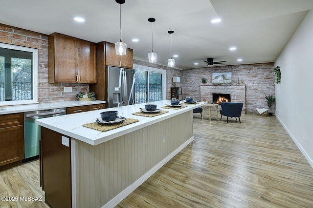 kitchen with a brick fireplace, a center island, ceiling fan, appliances with stainless steel finishes, and light wood-style floors