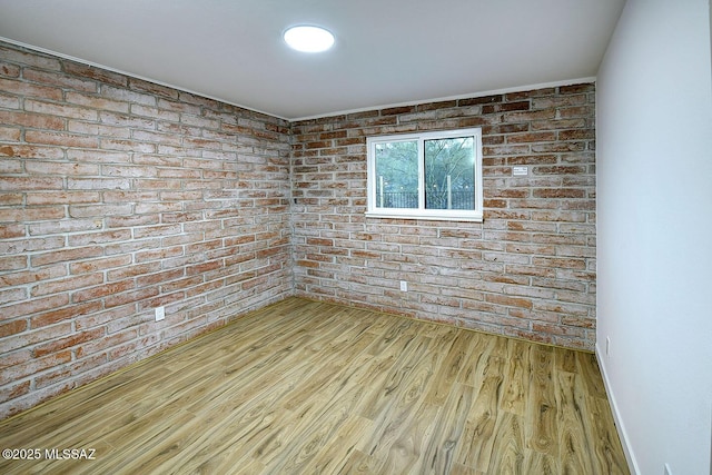 unfurnished room featuring wood finished floors, baseboards, and brick wall