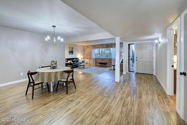 dining area featuring a brick fireplace, a notable chandelier, baseboards, and light wood-type flooring