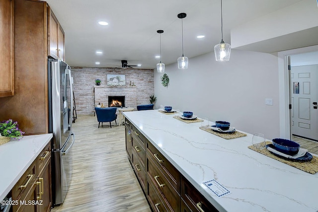 kitchen featuring light stone countertops, light wood finished floors, a fireplace, hanging light fixtures, and stainless steel fridge