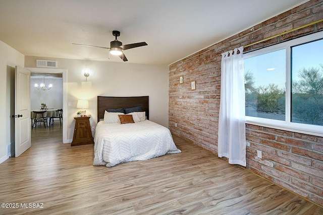 bedroom with visible vents, brick wall, baseboards, light wood-style flooring, and ceiling fan with notable chandelier