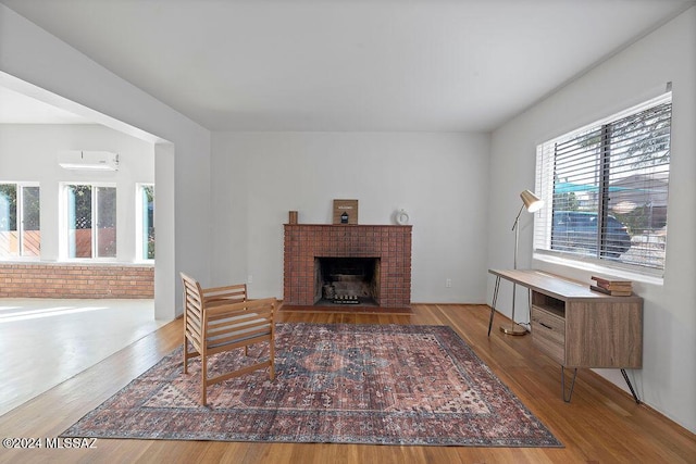 living room featuring a wall mounted AC, a fireplace, wood finished floors, and brick wall