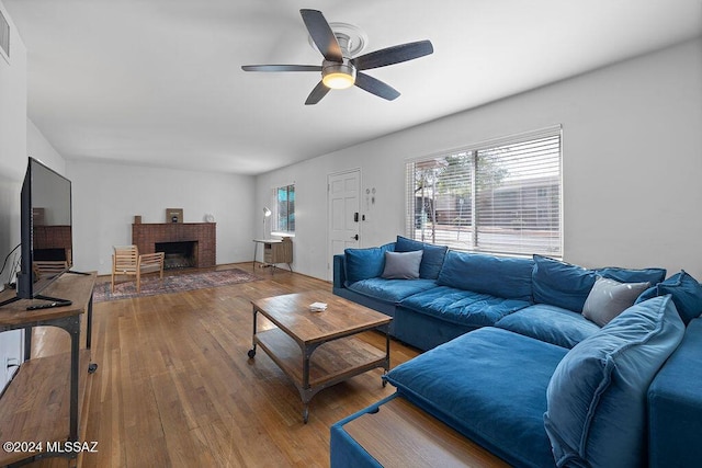 living area with plenty of natural light, a brick fireplace, wood finished floors, and a ceiling fan