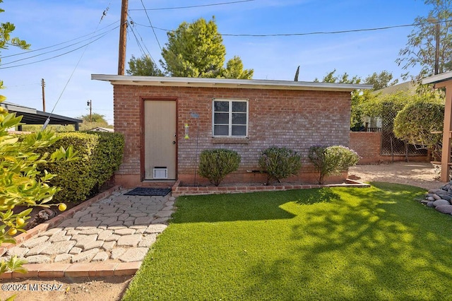 exterior space featuring a front yard, an outdoor structure, fence, and brick siding