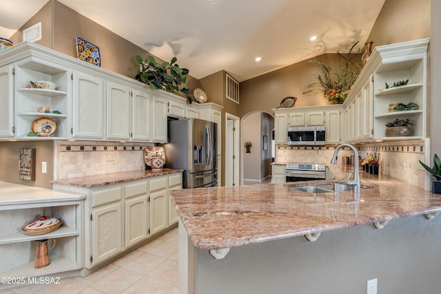 kitchen featuring open shelves, arched walkways, a sink, appliances with stainless steel finishes, and a peninsula