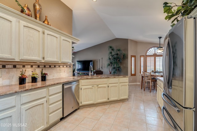 kitchen with cream cabinets, appliances with stainless steel finishes, a sink, lofted ceiling, and decorative backsplash
