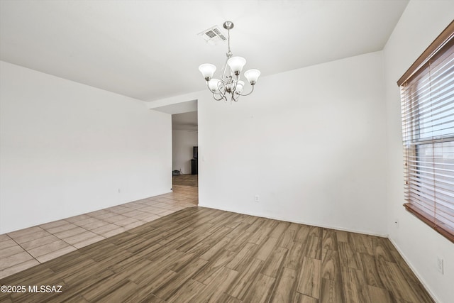 spare room featuring visible vents, an inviting chandelier, and wood finished floors