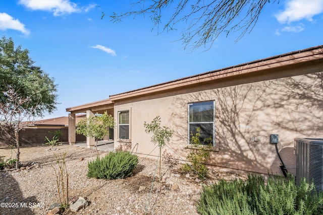 view of side of home featuring central air condition unit, stucco siding, a patio, and fence