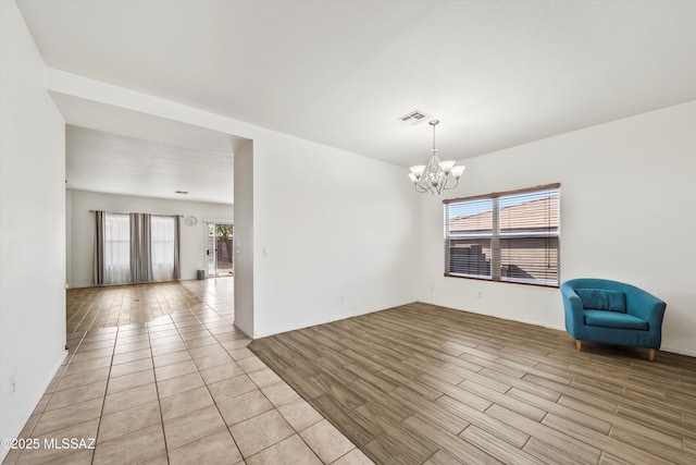 empty room with an inviting chandelier, light wood-style flooring, and visible vents