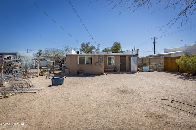 rear view of house featuring stucco siding and fence