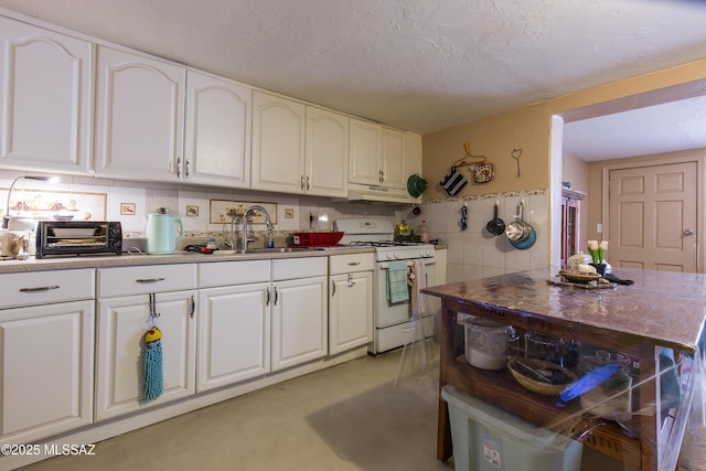 kitchen with under cabinet range hood, white range with gas cooktop, white cabinets, a textured ceiling, and a sink