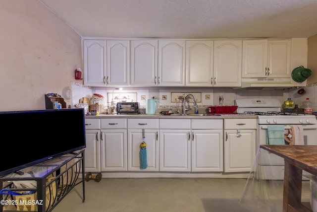 kitchen featuring white gas stove, a sink, under cabinet range hood, tasteful backsplash, and white cabinetry