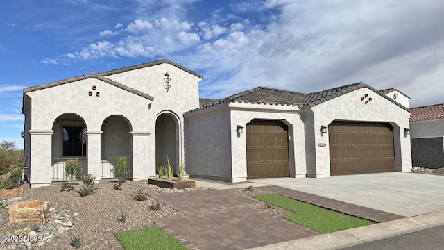 mediterranean / spanish-style home with a tiled roof, stucco siding, an attached garage, and decorative driveway