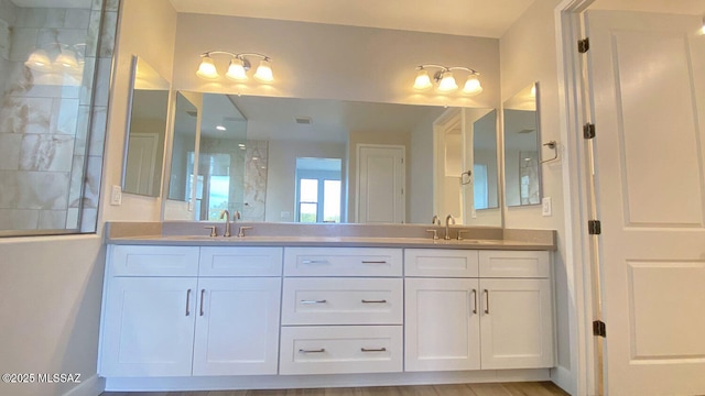 bathroom with a sink, double vanity, visible vents, and tiled shower