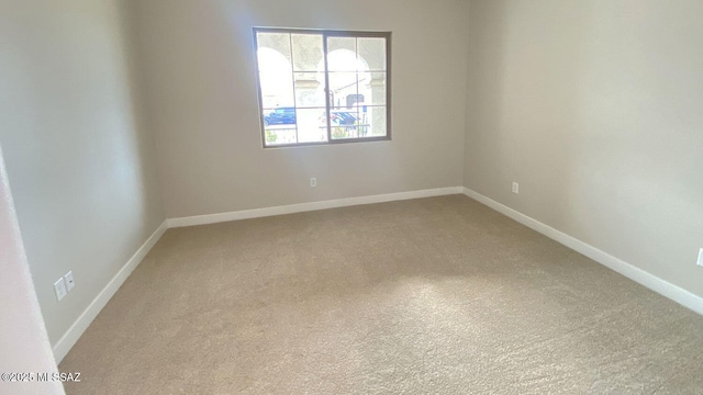 spare room with baseboards and light carpet