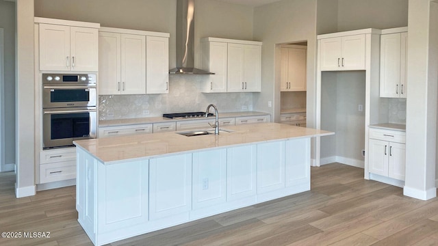 kitchen featuring a center island with sink, appliances with stainless steel finishes, wall chimney exhaust hood, and white cabinetry