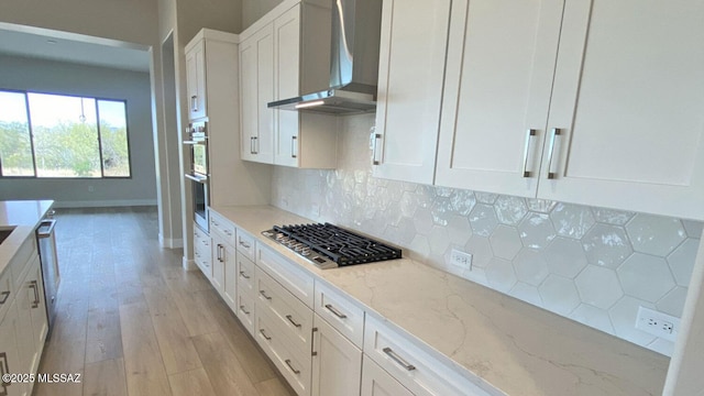 kitchen featuring backsplash, appliances with stainless steel finishes, white cabinetry, and wall chimney exhaust hood