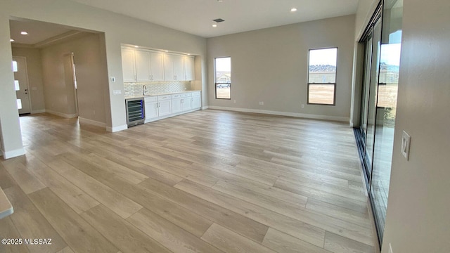 unfurnished living room with beverage cooler, recessed lighting, light wood-type flooring, and baseboards