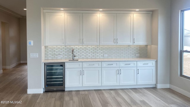 bar featuring wine cooler, tasteful backsplash, light wood-style floors, and a sink