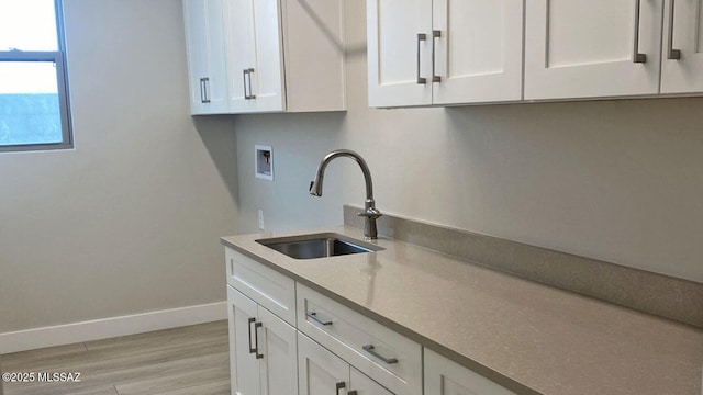 kitchen featuring a sink, baseboards, light wood-style flooring, and white cabinetry