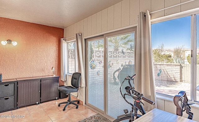 office area with light tile patterned floors, plenty of natural light, wood walls, and a textured wall