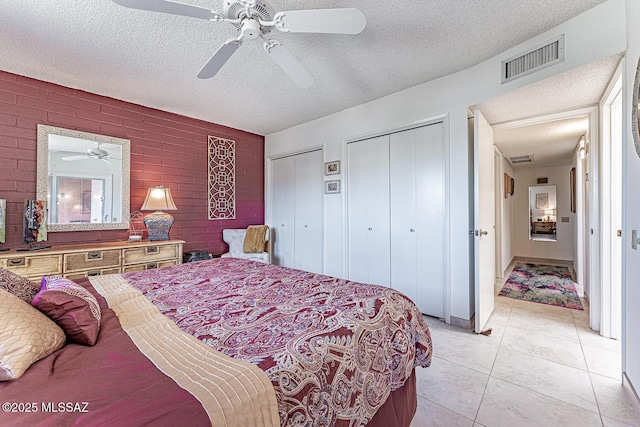 bedroom with visible vents, two closets, light tile patterned floors, a textured ceiling, and a ceiling fan