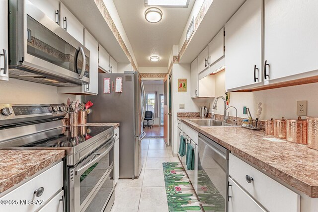 kitchen with a sink, white cabinetry, appliances with stainless steel finishes, and light tile patterned floors