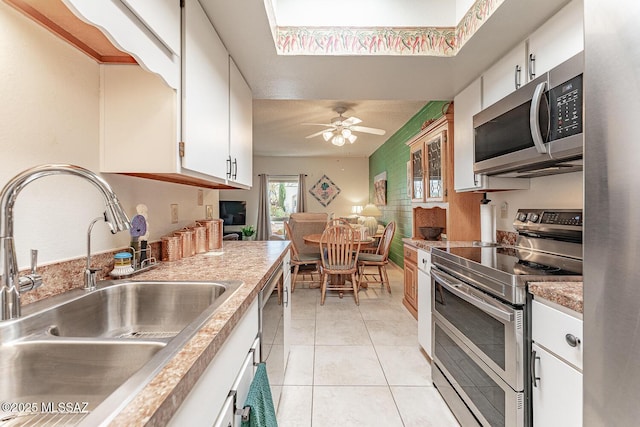 kitchen with a sink, stainless steel appliances, white cabinets, light tile patterned floors, and ceiling fan