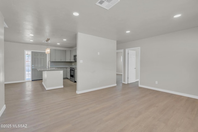 unfurnished living room featuring a sink, visible vents, baseboards, and light wood-style flooring