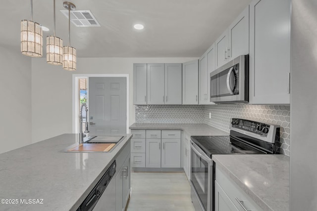 kitchen featuring visible vents, a sink, backsplash, appliances with stainless steel finishes, and light stone countertops