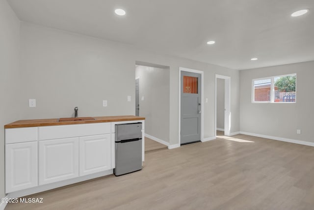 kitchen with light wood finished floors, butcher block countertops, recessed lighting, white cabinets, and a sink