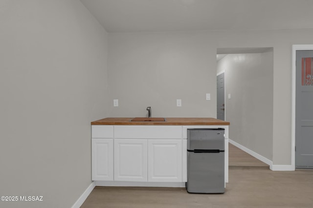 kitchen featuring white cabinets, wooden counters, freestanding refrigerator, and a sink