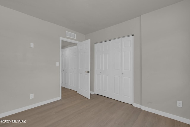 unfurnished bedroom featuring visible vents, baseboards, a closet, and wood finished floors