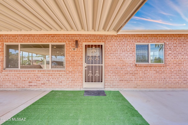 entrance to property featuring brick siding and a lawn