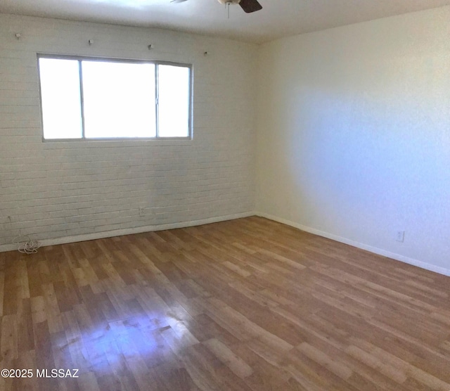 unfurnished room with wood finished floors, brick wall, a ceiling fan, and baseboards