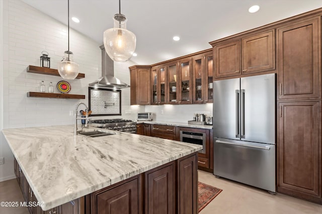 kitchen with tasteful backsplash, wall chimney range hood, decorative light fixtures, appliances with stainless steel finishes, and a peninsula