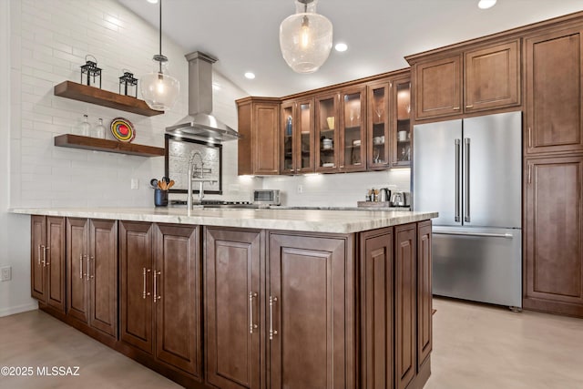 kitchen featuring wall chimney range hood, high end fridge, backsplash, and pendant lighting