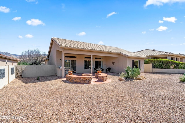 rear view of property featuring a tile roof, an outdoor fire pit, stucco siding, a fenced backyard, and a patio