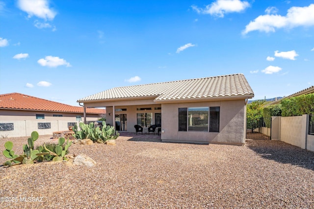 rear view of house with stucco siding, a tiled roof, a fenced backyard, and a patio