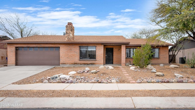 ranch-style home with brick siding, central air condition unit, concrete driveway, a chimney, and a garage