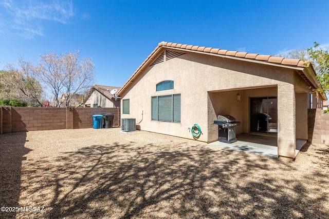 rear view of house with a tiled roof, central AC unit, stucco siding, a fenced backyard, and a patio