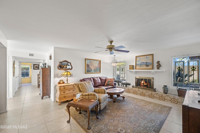living room with a ceiling fan, a glass covered fireplace, light tile patterned flooring, and a wealth of natural light