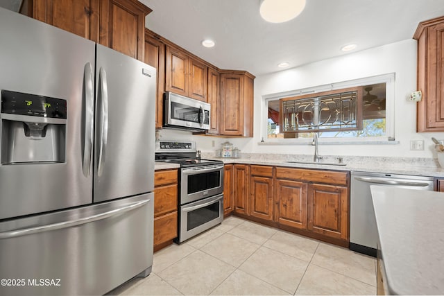 kitchen with brown cabinets, stainless steel appliances, light tile patterned floors, and a sink