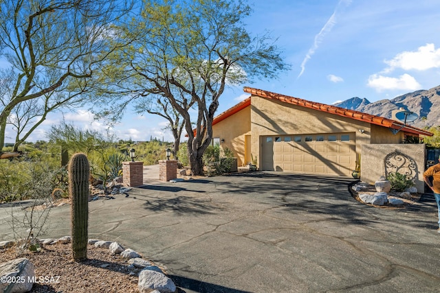 view of property exterior featuring stucco siding, a tiled roof, an attached garage, a mountain view, and driveway