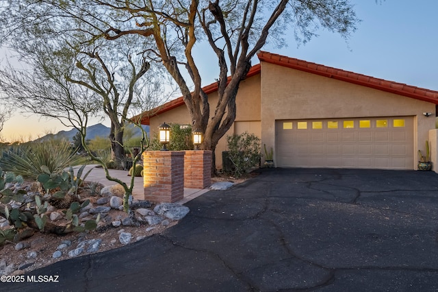 mid-century modern home featuring a garage, stucco siding, a tiled roof, and aphalt driveway