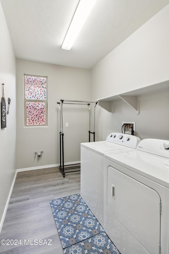 washroom with laundry area, washing machine and dryer, baseboards, and light wood-style floors