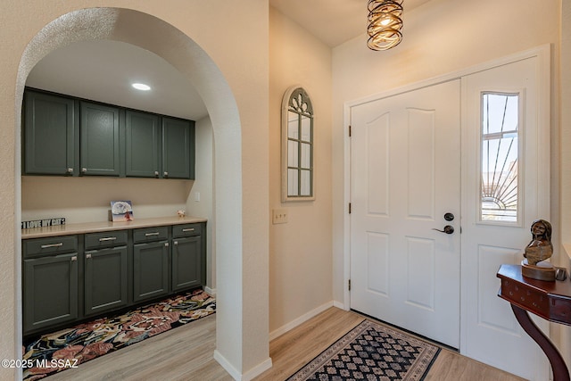 foyer entrance featuring arched walkways, baseboards, and light wood finished floors