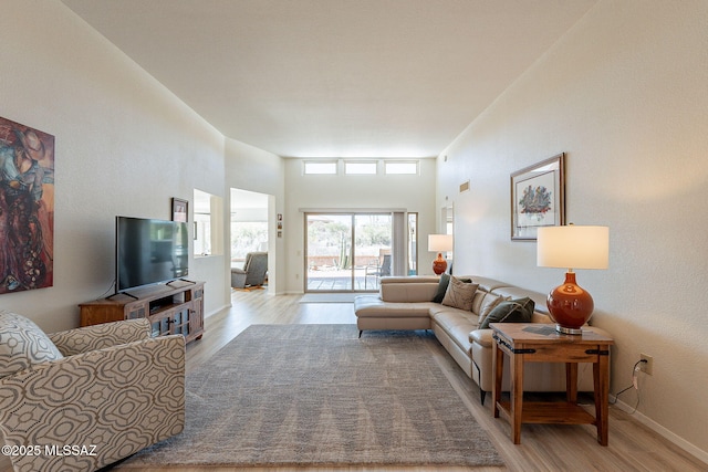 living room featuring baseboards, light wood-type flooring, and a high ceiling