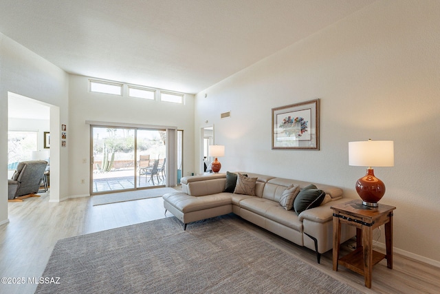 living room with a high ceiling, light wood-style flooring, visible vents, and baseboards