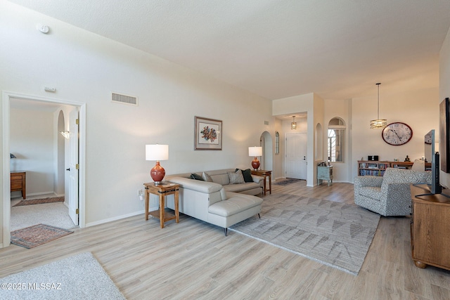 living room featuring visible vents, arched walkways, baseboards, and light wood finished floors